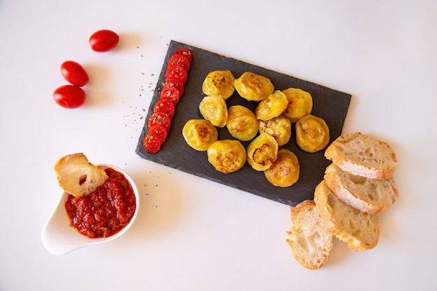 Russian food pelmeni, fried meat dumplings on stone plate, with tomates, bread and red sauce. Top view, flat lay.