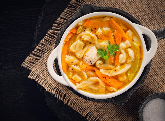 Russian homemade chicken soup with noodles and vegetables in a white plate on a black background