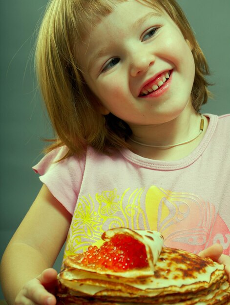 Foto la bambina russa mangia i pancake con il caviale rosso