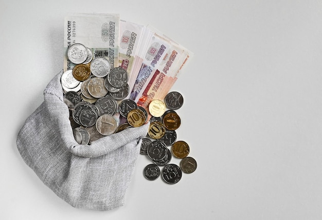 Российские деньги в мешке, монеты и банкноты на белом фоне, вид сверху, копия пространства