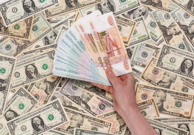Российские деньги номиналом в одну и пять тысяч рублей держат в руках на фоне доллара США
