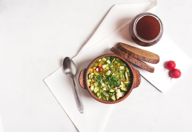 Russian okroshka with bread kvass and vegetables in a clay cup on a gray