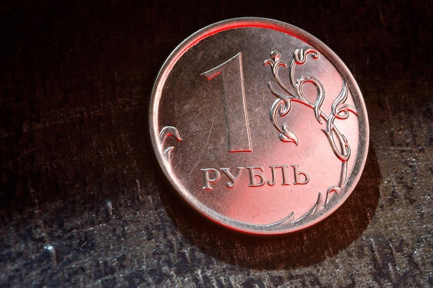 Российская монета в один рубль лежит на темном металлическом фоне крупным планом