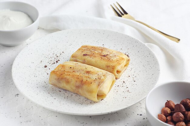 Russian pancakes are on a saucer on the table. Nearby are a towel, a fork and nuts. This is breakfast