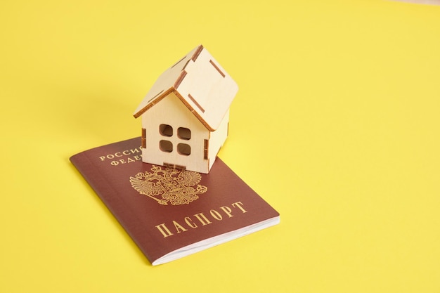 노란색 배경에 러시아 여권과 나무 장난감 집 부동산 구매 개념