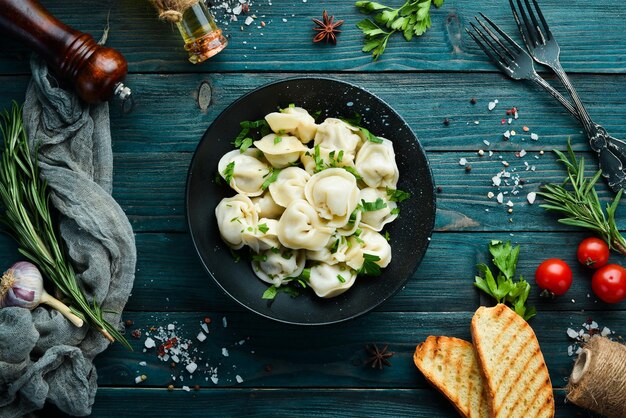 Russian pelmeni meat Dumplings with greens in a black plate Russian traditional cuisine Top view Free copy space