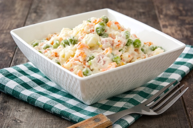 Russian salad in bowl on rustic wooden