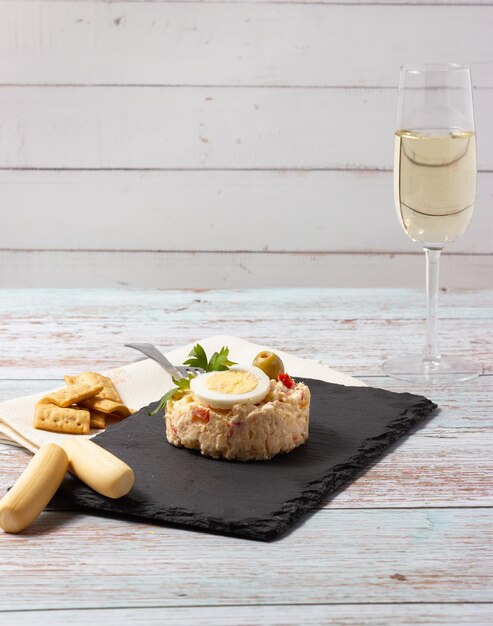 Photo russian salad typical spanish tapa on a black slate plate with a cup of white sherry wine