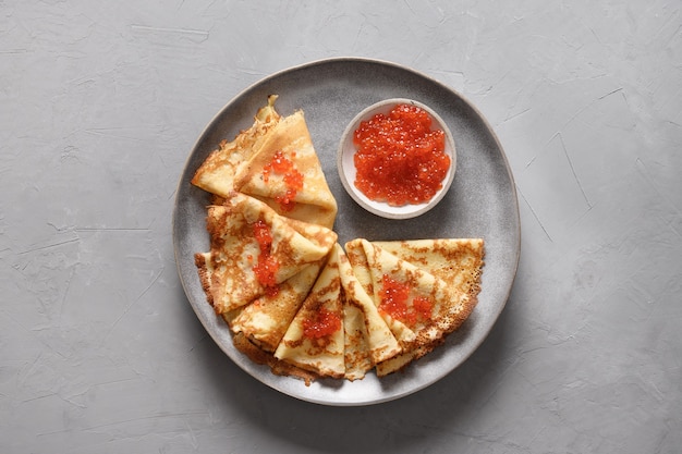 Russian thin pancakes with red caviar on grey background