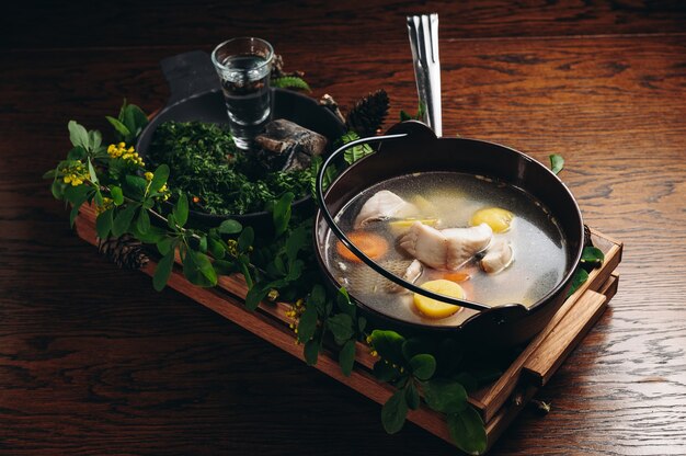 Russian traditional fish soup in a bowl  ukha served with ember and vodka on wooden board Fish broth Traditional cuisine in Russia