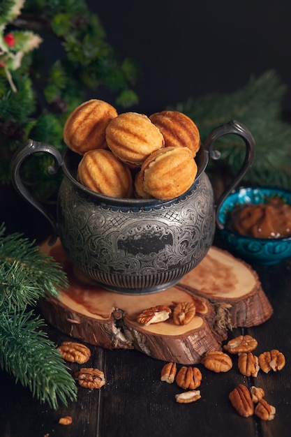 Russian traditional homemade cookies Nuts - Oreshki with condensed milk on an vintage jar on a wooden stand surrounded by spruce branches and scattered nuts.