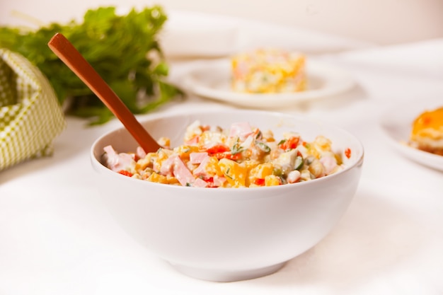 Russian traditional salad Olivier with vegetables and meat in the white bowl.
