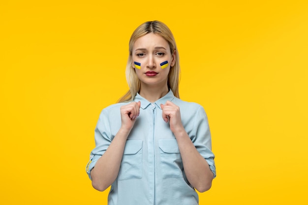 Russian ukrainian conflict cute girl yellow background with ukrainian flag on cheeks holding fists