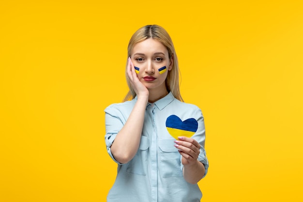 Russian ukrainian conflict cute girl yellow background with ukrainian flag on cheeks holding heart