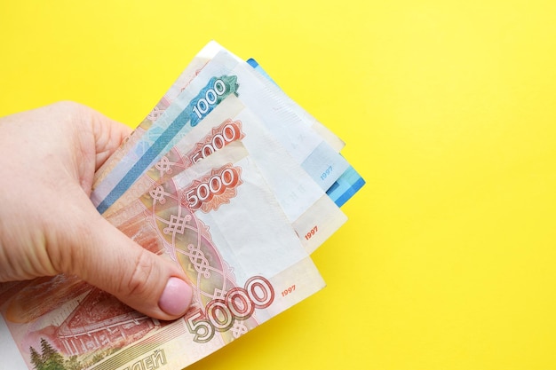 Russische roebelbankbiljetten in een vrouwelijke hand op een gele achtergrond Kopieer de ruimte