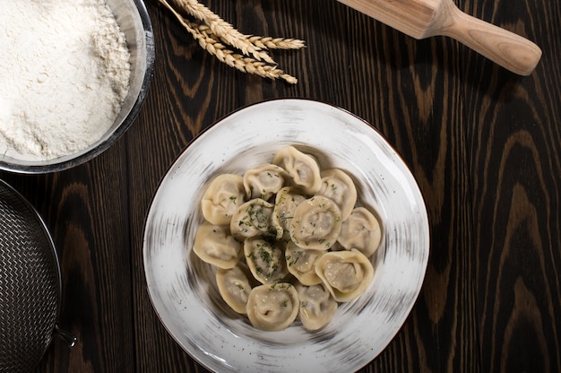 Russische traditionele pelmeni met vlees op een witte plaat. Tarwe aren, op een houten bord