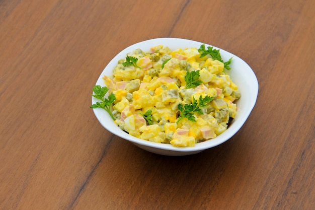 Russische traditionele salade olivier met groene erwt, eieren, ingelegde komkommer, aardappel, worstjes en mayonaise op houten tafel