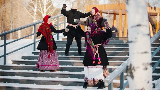Russische volksmannen en -vrouwen in vilten laarzen dansen op de trappen in het winterpark