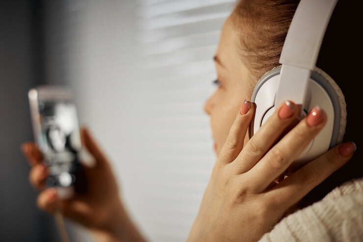 Rust en ontspanning, jonge blanke vrouw luisteren naar muziek in koptelefoon met behulp van een smartphone zittend op de vensterbank.