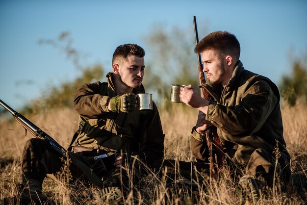 Rust voor echte mannen concept Jagers met geweren ontspannen in de natuuromgeving Jagen met vrienden hobby vrije tijd Jagers vrienden genieten van vrije tijd Jagers tevreden met vangst drankje verwarmende drank