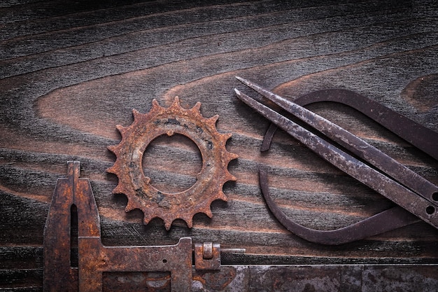 Rusted antique measuring calipers with gear wheel on vintage dark wooden background construction concept