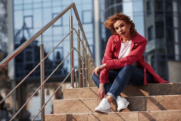 Rusten en fotoshoot doen. Volwassen mooie vrouw in warme rode jas wandelt in het weekend door de stad