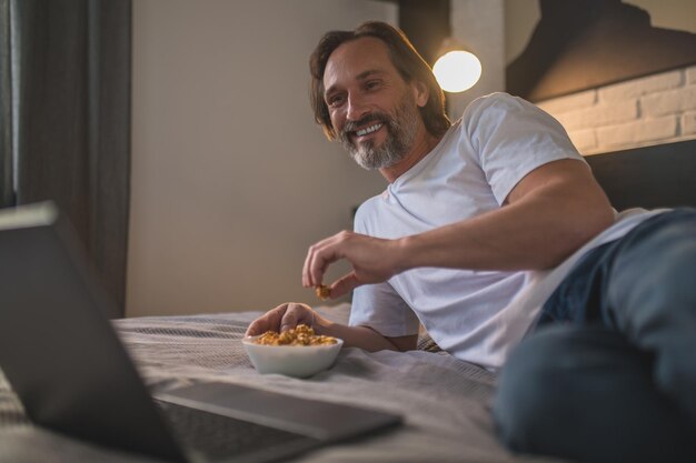 Rusten. Man rust na het werk en eet snacks terwijl hij iets online kijkt