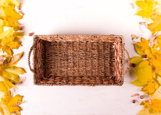 Photo rustic basket, autumn leaf border on white background, top view