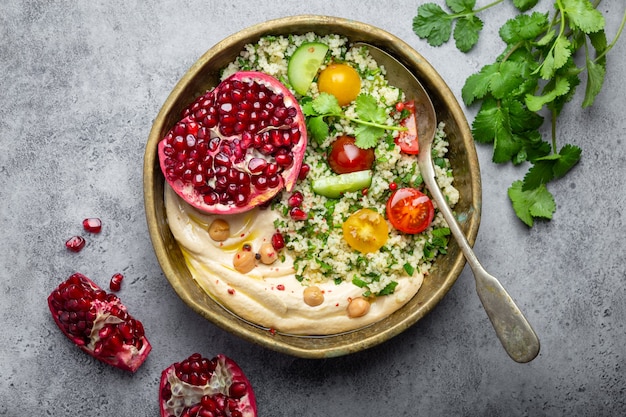 Rustic bowl with couscous salad with vegetables, hummus and fresh cut pomegranate. Middle eastern or Arab style meal with seasonings and fresh cilantro. Beautiful and healthy Mediterranean dinner