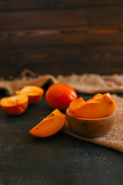 Rustic compositie met verse persimmons in een houten schaal en op een donkere textuur achtergrond geaccentueerd door burlap Ideaal voor seizoensgebonden culinaire en rustieke lifestyle thema's