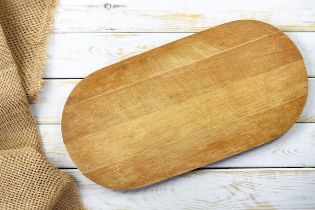 Rustic culinary template top view of a white vintage wooden table with an empty cutting board and burlap sack