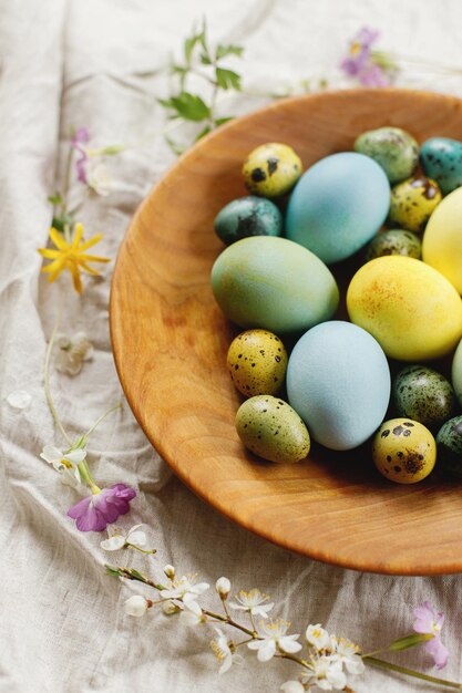 Rustic easter still life Stylish easter eggs and blooming spring flowers in wooden bowl on linen fabric Happy Easter Natural painted eggs and blossoms on rural table