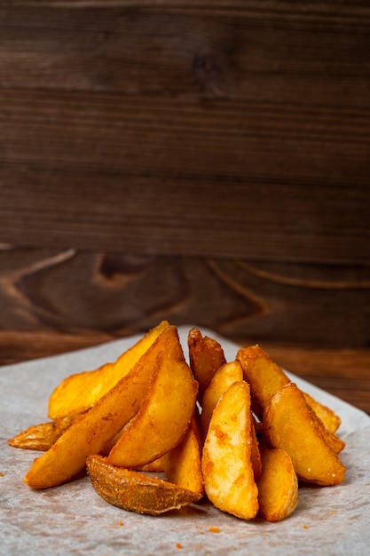 Rustic fried potatoes on paper and wooden background.