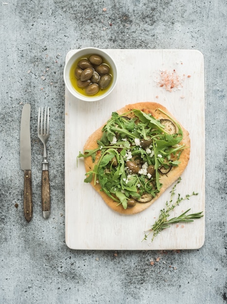 Rustic homemade pizza with eggpant, cheese, olives and arugula on  white wooden serving board