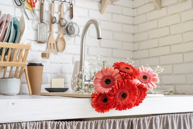 Rustic kitchen interior with white brick wall and white wooden shelves red and pink gerbera daisies