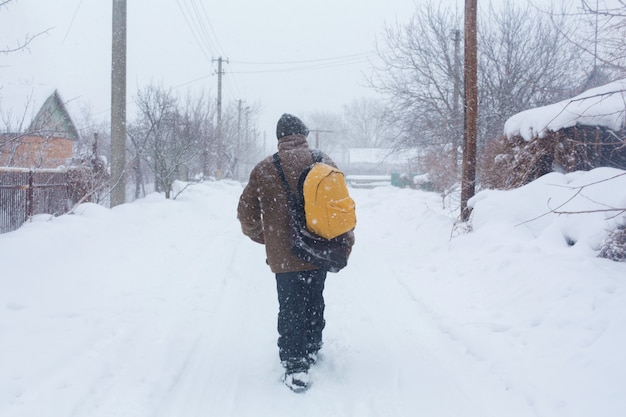 素朴な男が冬に黄色のバックパックを持って通りを歩いています。吹雪