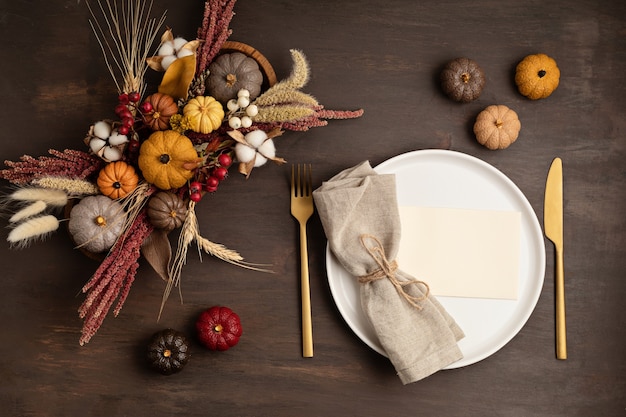 Rustic menu mockup with plate and autumn table decoration. Floral interior decor for fall holidays with handmade pumpkins. Holiday dinner concept. Flatlay, top view