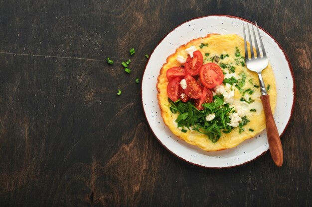 Rustic omelette or frittatas with green onions cheese mozzarella green arugula and tomatoes on old wooden dark background Healthy food concept Breakfast Copy space Top view Mock up