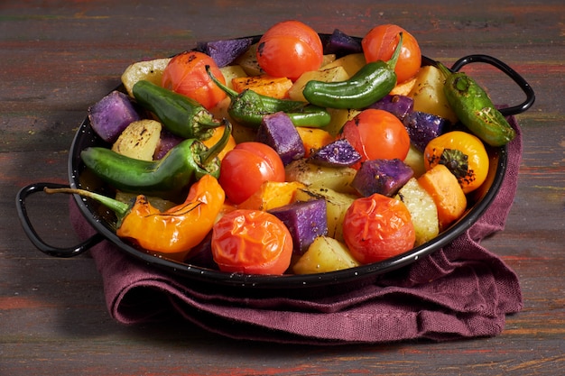 Rustic, oven baked vegetables in baking dish. Seasonal vegetarian vegan meal on dark wooden  with linen towel