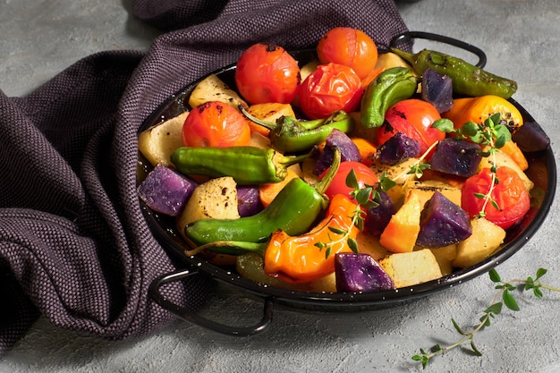 Rustic, oven baked vegetables in baking dish. Seasonal vegetarian vegan meal on light concrete