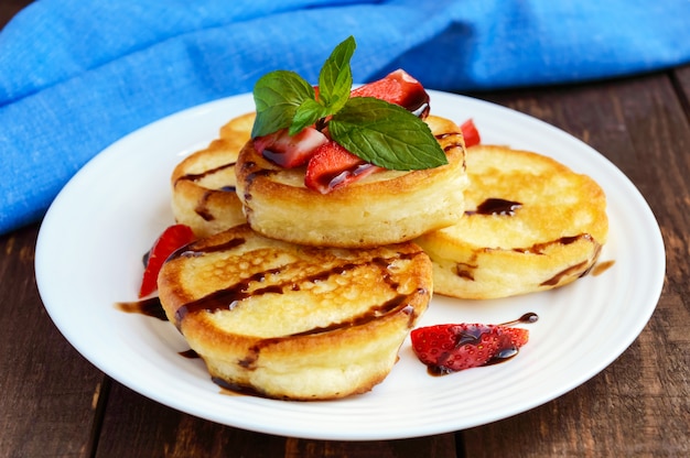 Rustic pancakes with fresh strawberries and chocolate on a white plate