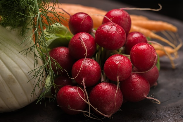 Photo rustic set of radishes along with other vegetables on a table.