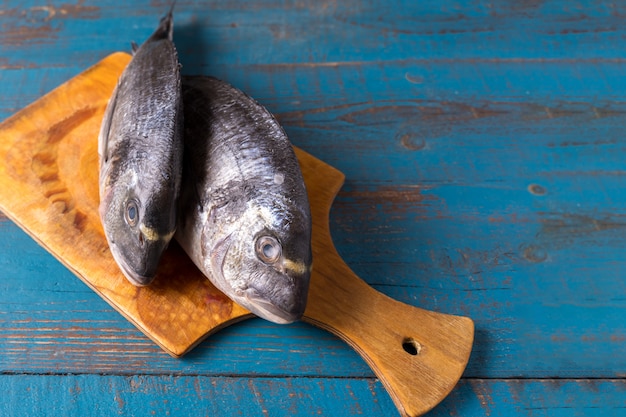 素朴なスタイル。魚のエサ。古い青い木製の背景とテキストのコピースペースにニシンの魚。