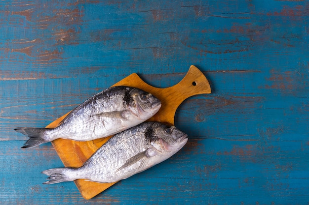 素朴なスタイル。生の魚の食べ物。古い青い木製の背景とテキストのコピースペースにまな板の上のニシンの魚。