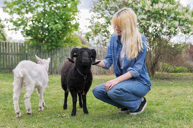 Adolescente della giovane donna della piccola fattoria degli animali di stile rustico gioca toccando l'ariete nero e la giovane capra bianca