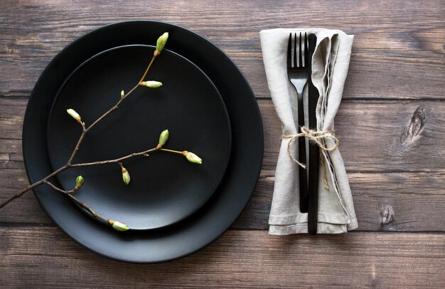 Rustic table setting Elegant empty black plate cutlery on linen napkin and natural tree branch on rustic planked wood