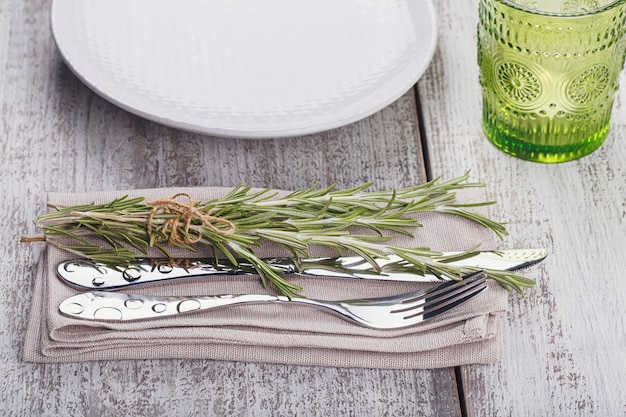 Rustic table setting with rosemary on light wooden table with copyspace. Holidays decoration on Provence style. Romantic dinner.