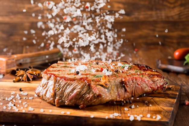 a rustic table with a large steak roasted with smoke spices herbs and rock salt falling two