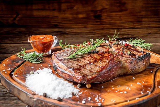 a rustic table with a large steak roasted with smoke spices herbs and rock salt sauce barbecue