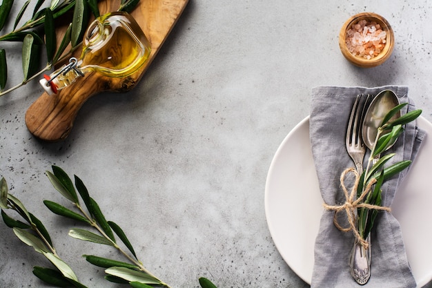 Rustic vintage set of cutlery. Plate with grey linen napkin, fork and spoon, olive tree branch over rustic concrete gray old. Fall holiday table decoration setting. 